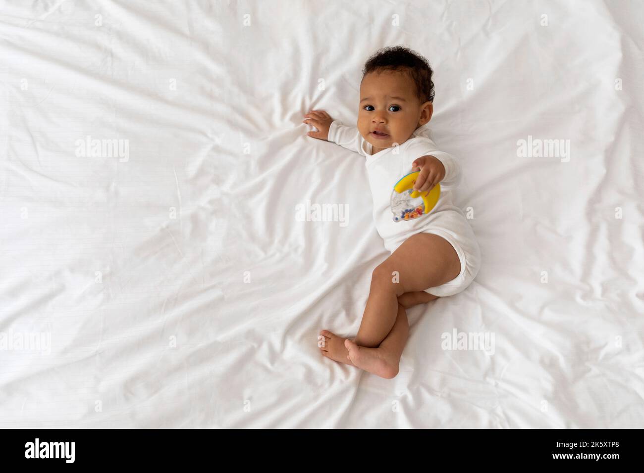 Cute Black Baby Playing With Toys While Relaxing On Bed At Home Stock Photo