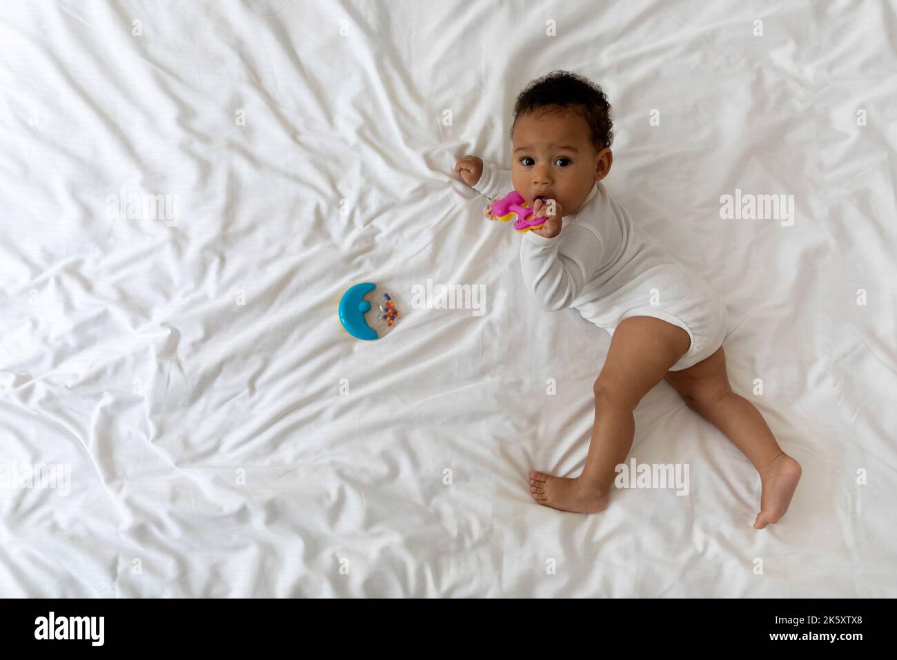 Cute Black Baby Relaxing On Bed And Playing With Toys Stock Photo