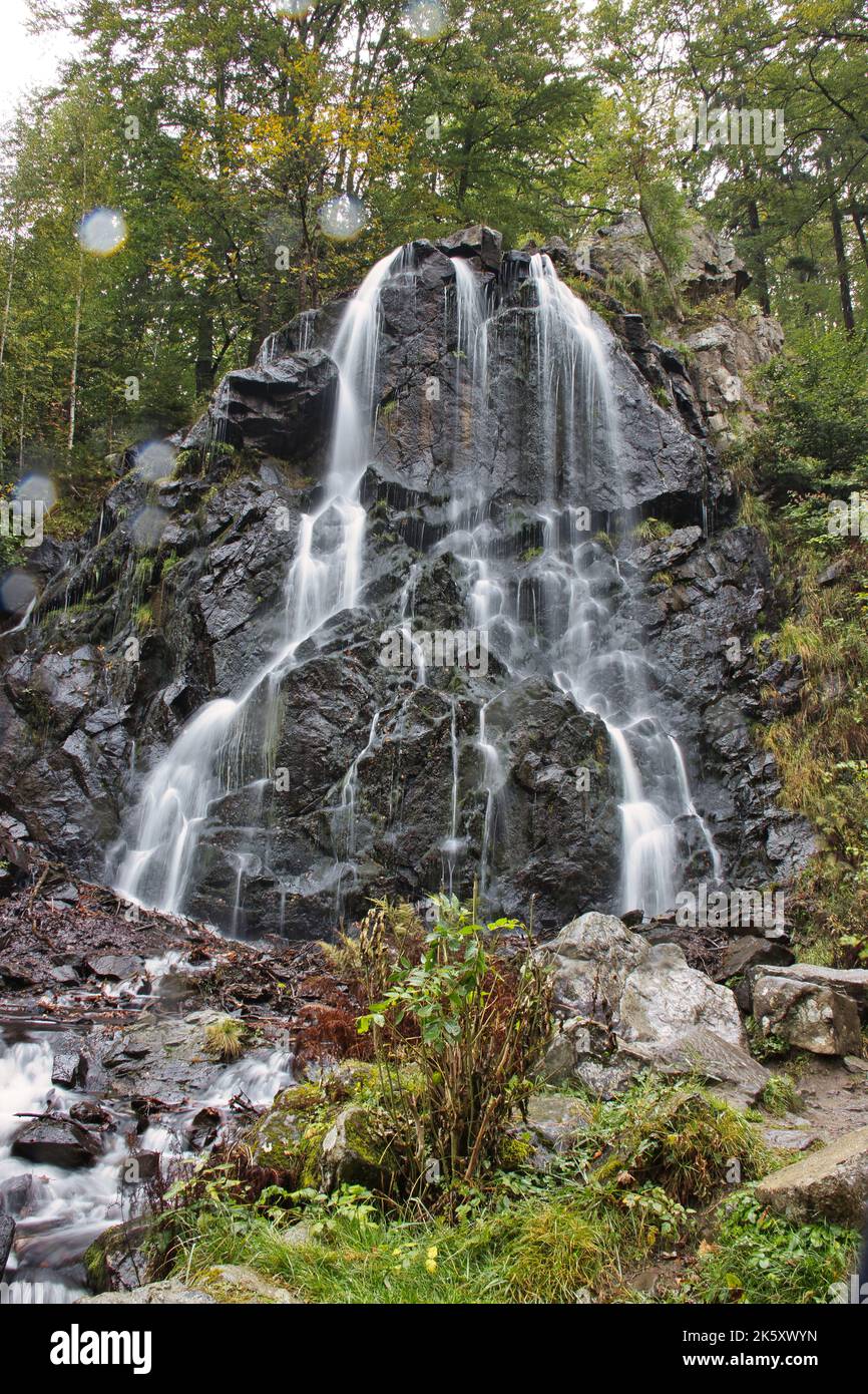 A vertical shot of a waterfall flowing down the rocks covered with ...
