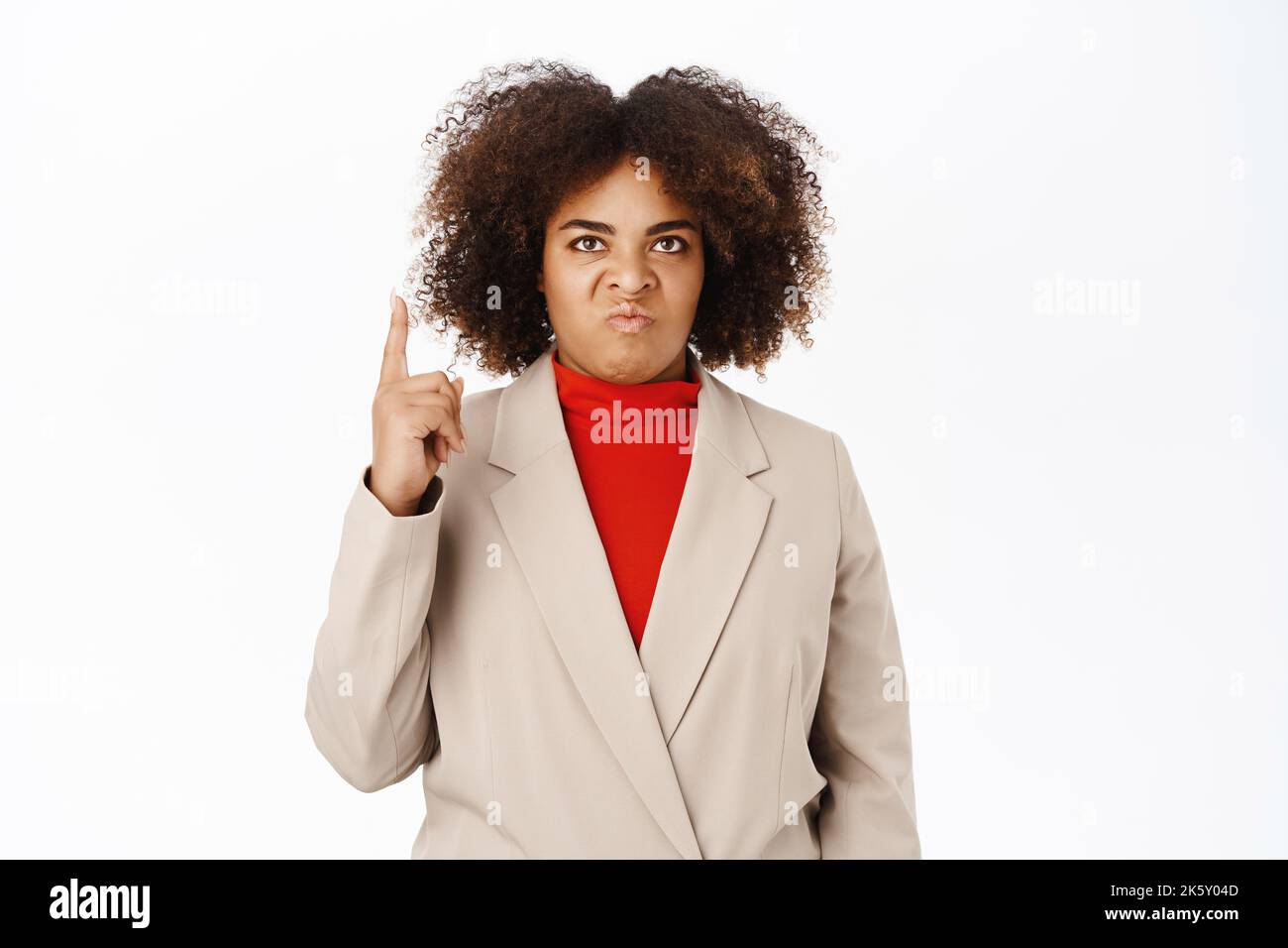 Angry businesswoman looks up, points at top with jealous, annoyed face