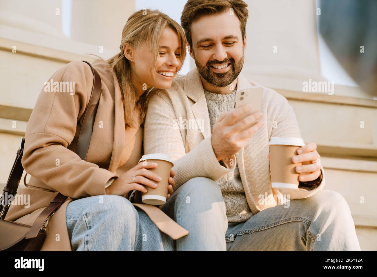 White romantic couple using cellphone and drinking coffee during date outdoors Stock Photo