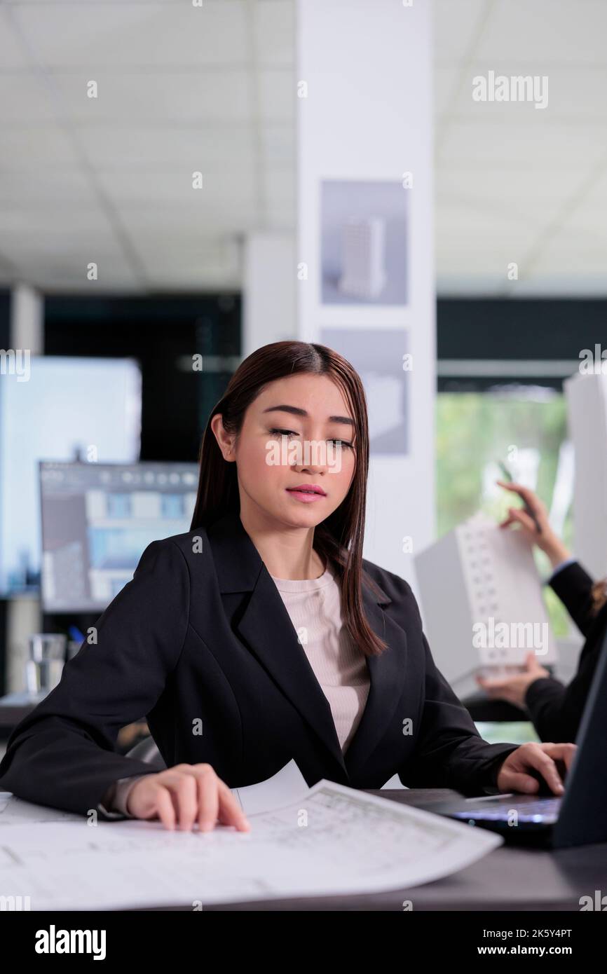 Asian architect working with project blueprints in coworking space