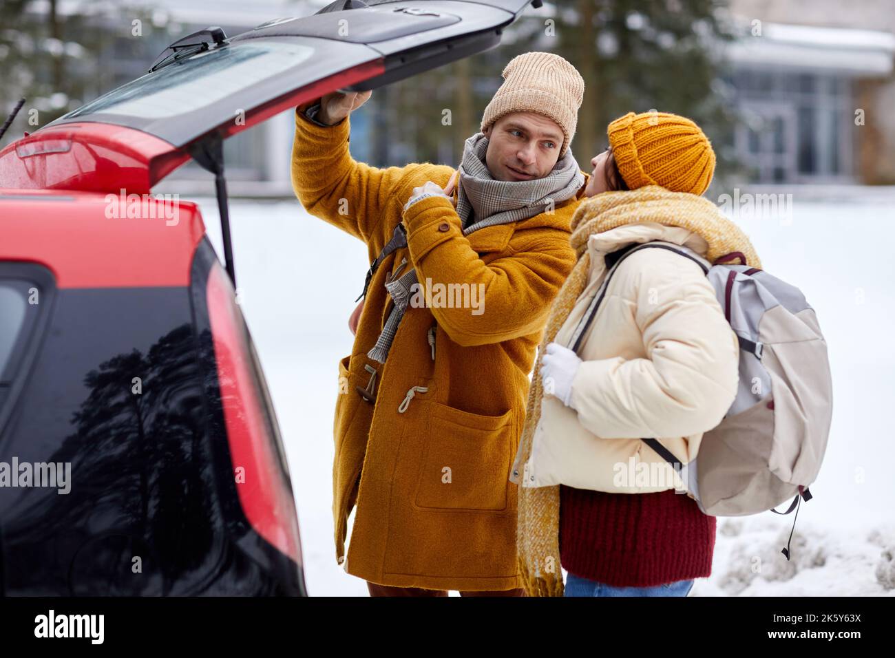 Side view portrait of young couple opening car trunk in winter while travelling for holidays Stock Photo