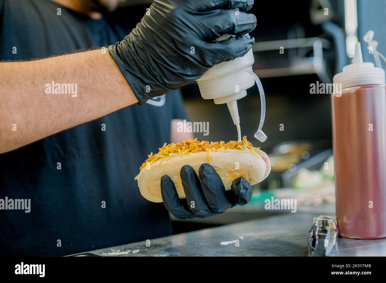 Unrecognizable street food vendor pouring sauce on hot dog Stock Photo