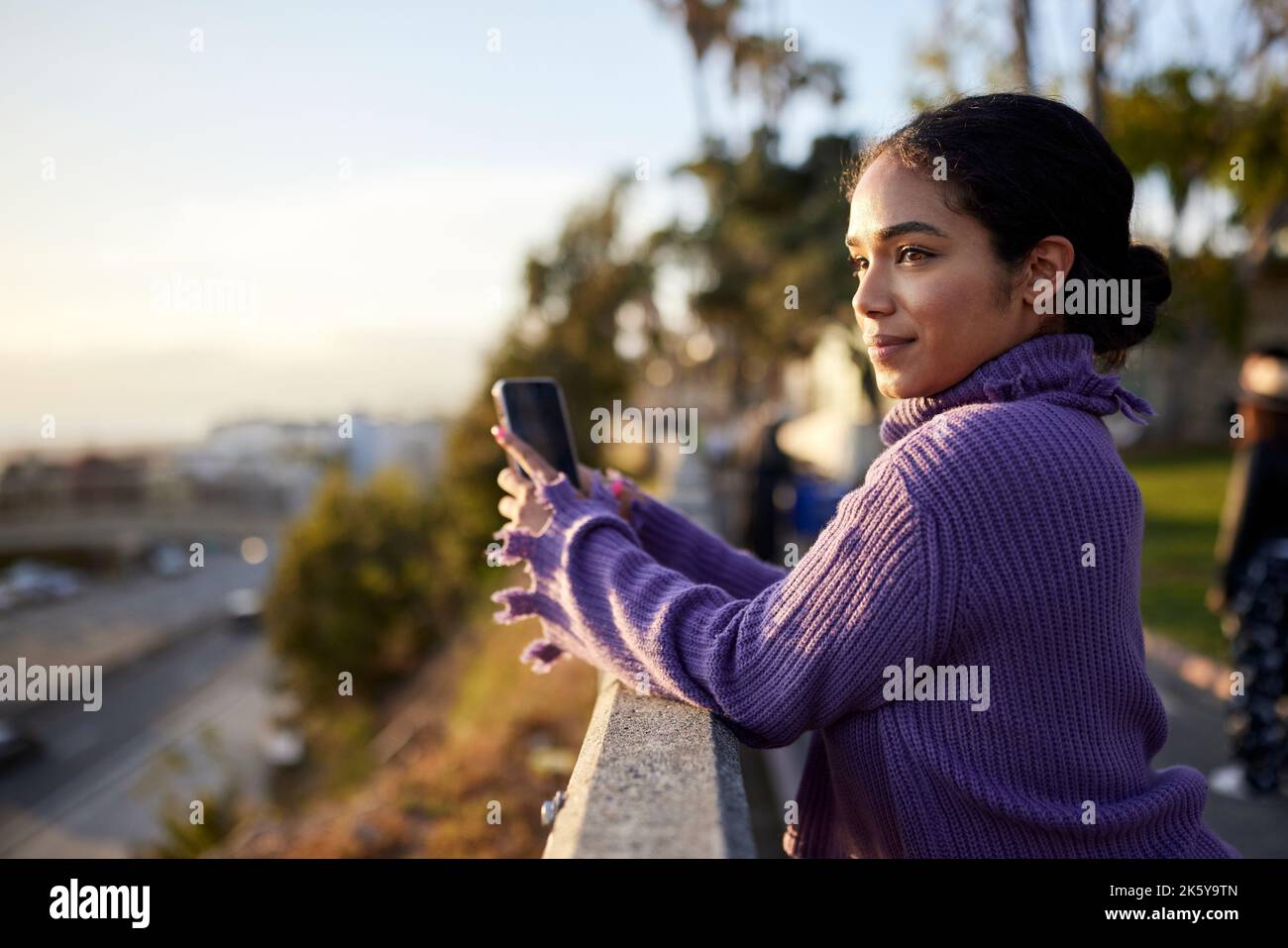 Contemplative woman with smart phone standing by railing Stock Photo