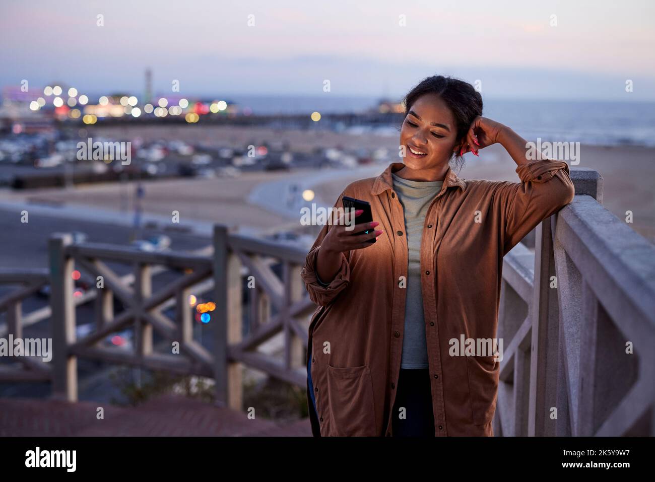 Smiling woman using smart phone leaning on railing Stock Photo