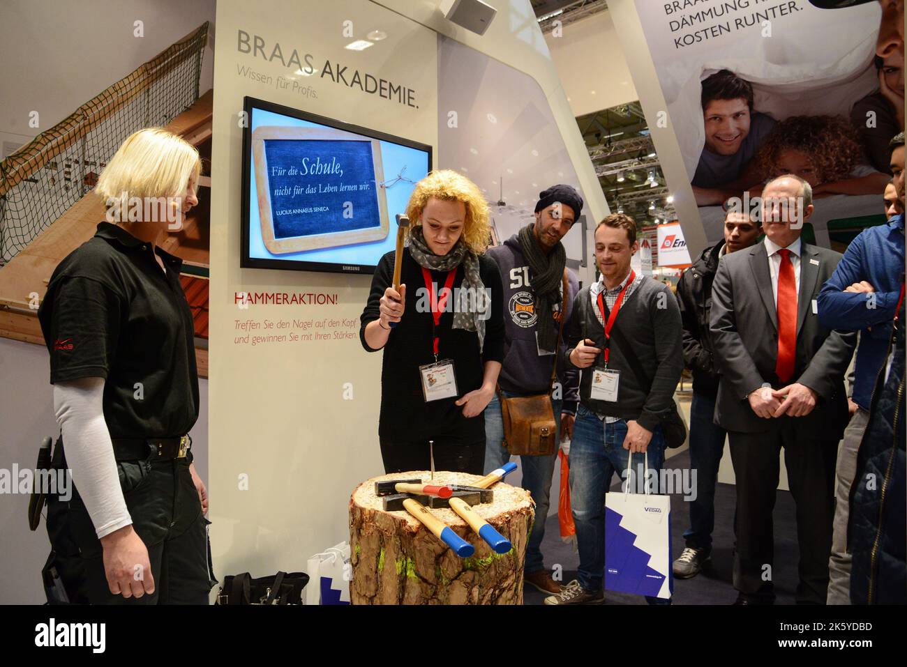 02-20-2014 Cologne, Germ Stunning blondes try to hammer a huge nail with a hammer at the booth of the company that produces these hammers Stock Photo