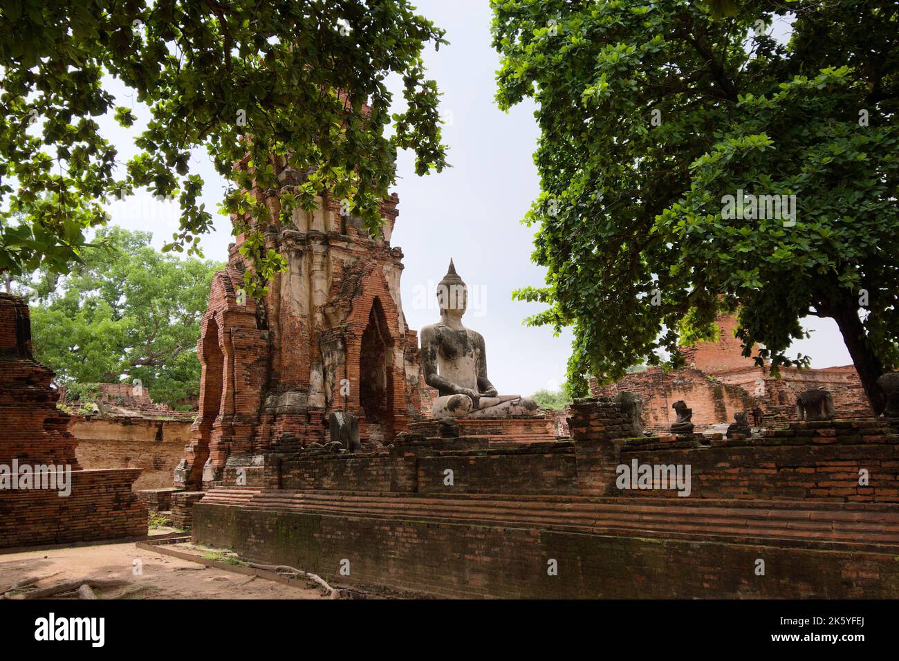 Seated Buddha in earth touching pose and restored ruins of a satellite vihara or monastic hall at Wat Mahathat, Ayutthaya Historical Park Stock Photo