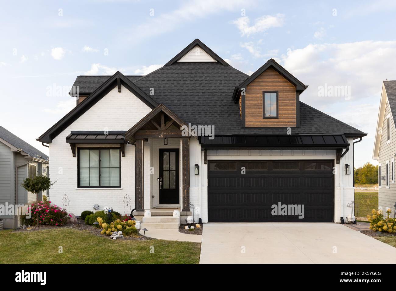 A beautiful, modern farmhouse home with a white brick and wood siding, black roof, and wooden ...