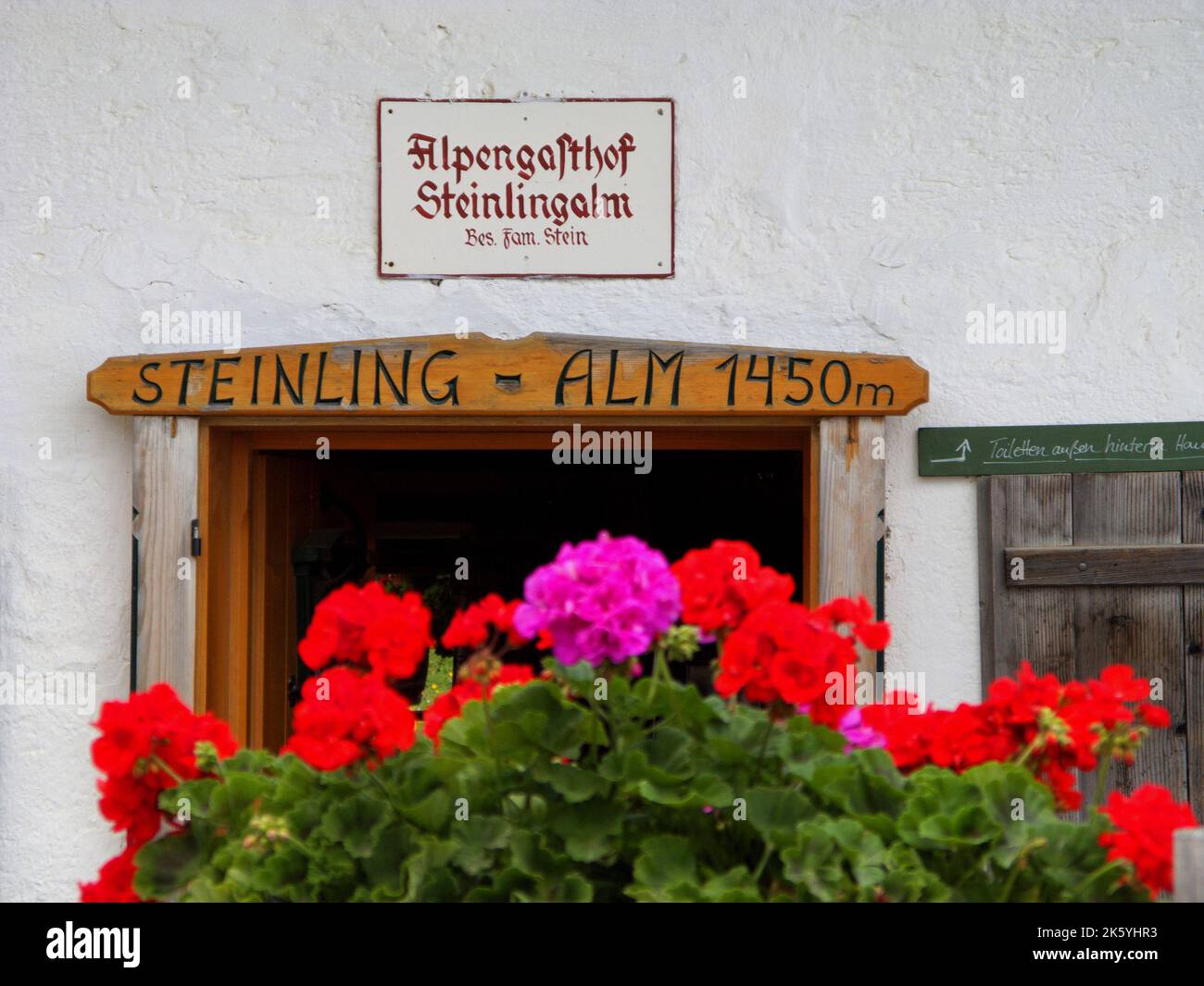 Entrance of alpine restaurant 'Steinling Alm' on kampenwand mountain, Chiemgau, and red Geraniums in foreground, Bavaria, Germany. Eingang zum Alpenga Stock Photo