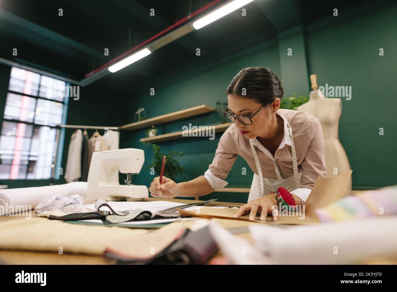 Asian fashion woman designer drawing design sketch. Female designer working in her fashion studio. Stock Photo
