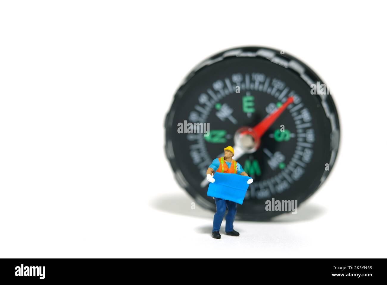 Miniature people toy figure photography. Project location concept. A construction worker with blueprint building standing with compass. Isolated on wh Stock Photo