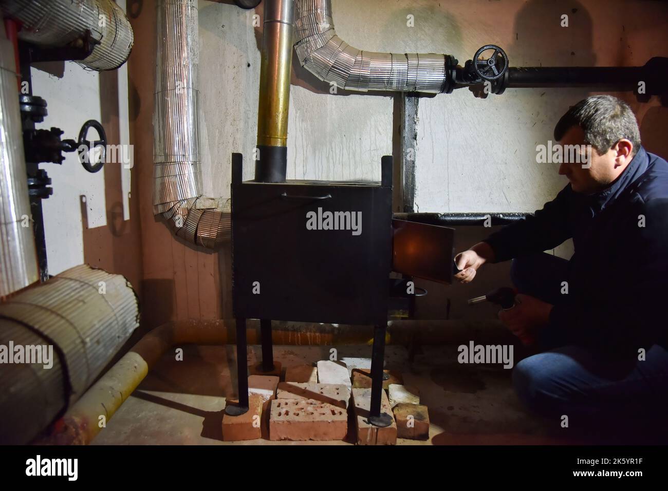 A man lights a metal stove in the basement of a house that serves as a