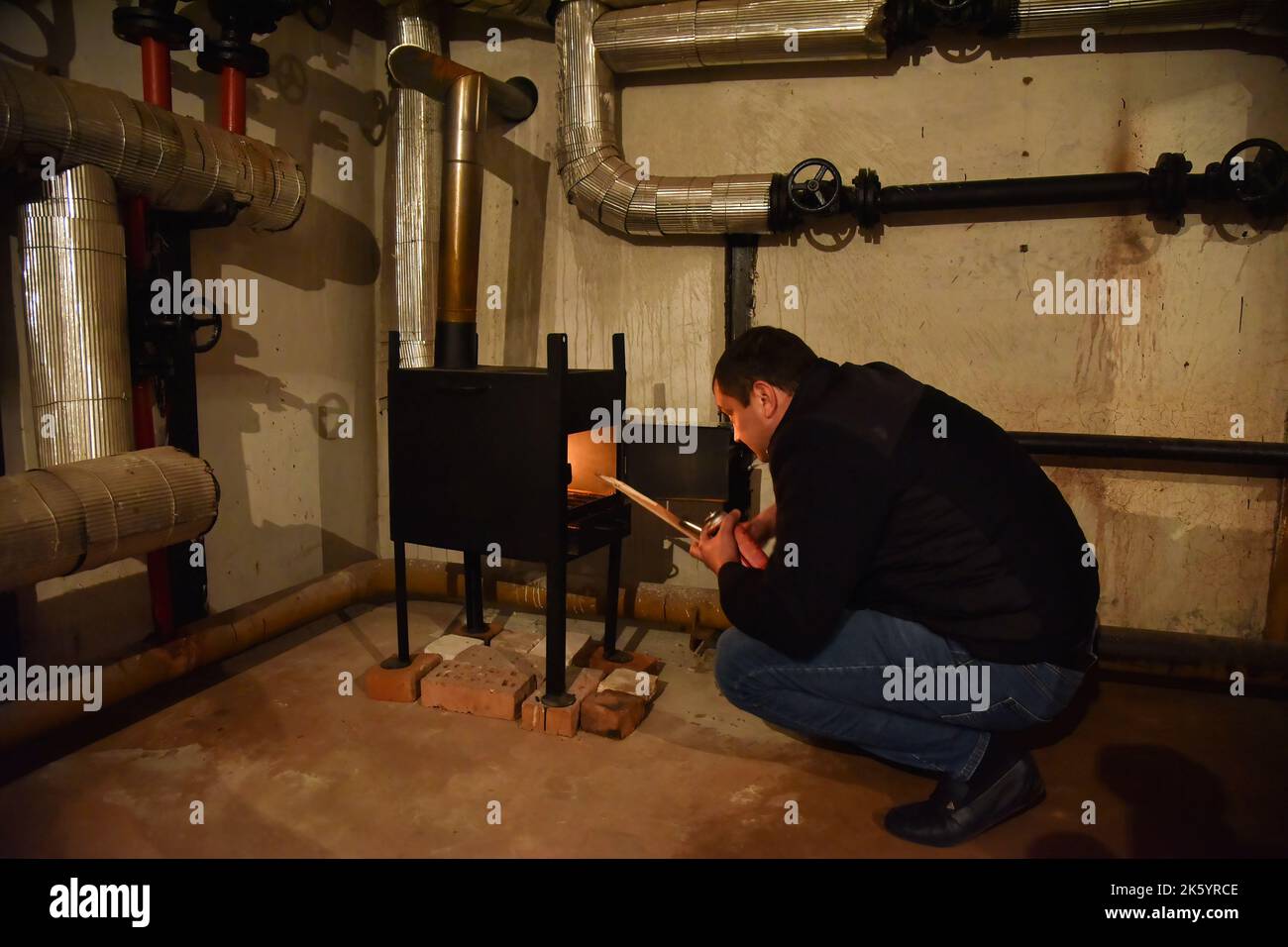 A man lights a metal stove in the basement of a house that serves as a