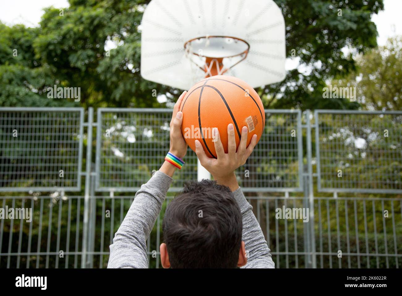 Man with a rainbow bracelet throwing a ball to the basket in a