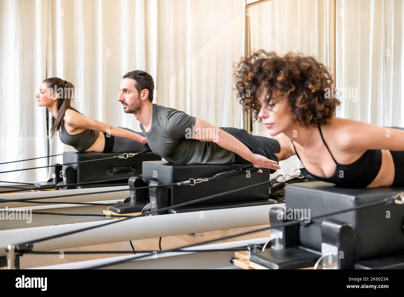 Male and female athletes in activewear doing thoracic extension exercise on box on reformer