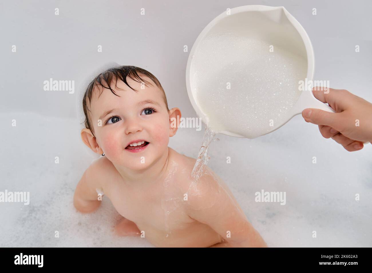 A mother washes a child sitting in a white tub with soap suds. Mom s