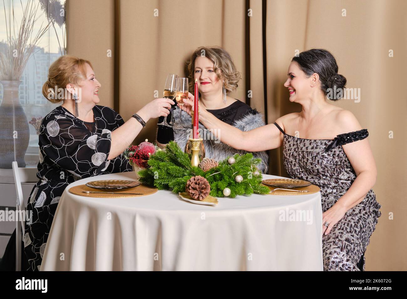 Three juyful middle age women celebrating christmas sitting behind the festive table Stock Photo