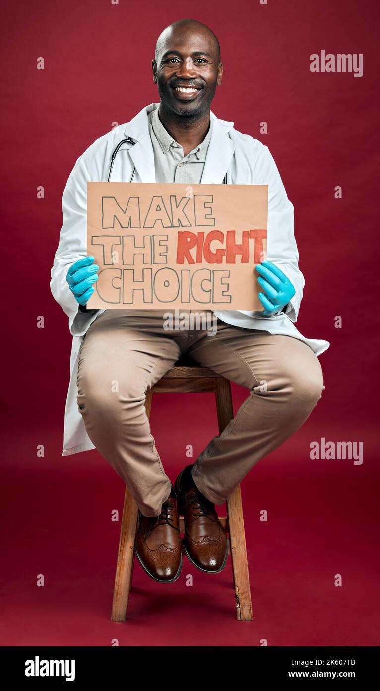 African american covid doctor holding and showing poster. Full length portrait of smiling black physician isolated against red studio background with Stock Photo