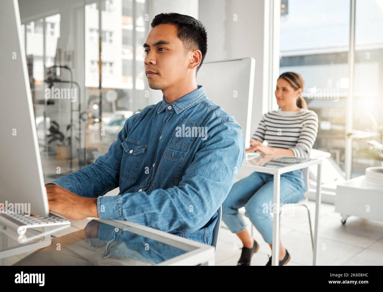Young focused asian businessman using a desktop computer in an office at work. Serious chinese male businessperson typing an email at a desk. Business Stock Photo