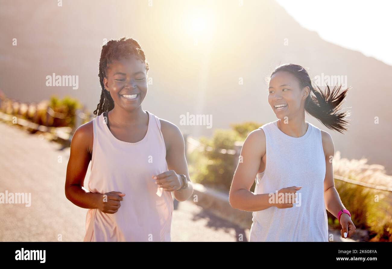 Two happy young female athletes out for a run on a mountain road on a sunny day. Energetic young women running outdoors to help their bodies in shape Stock Photo