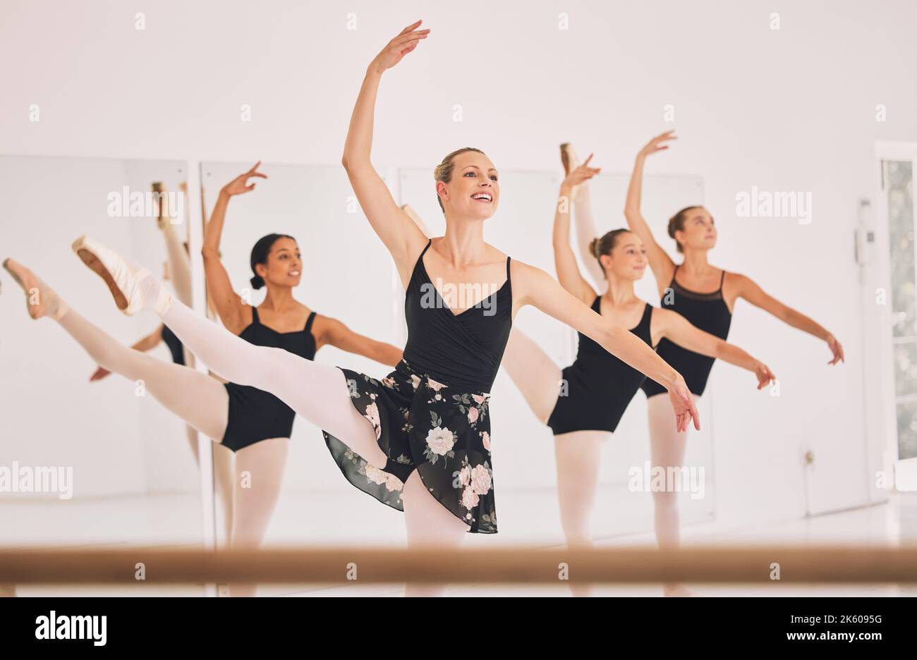 Young woman dance instructor teaching a ballet class to a group of a children in her studio. Ballerina teacher working with girl students, preparing Stock Photo