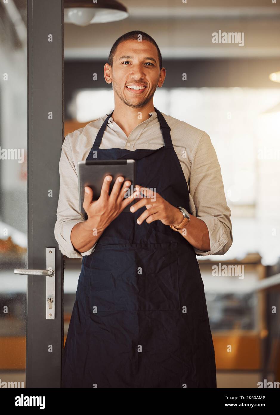 Businessman using a digital tablet in his cafe entrance. Bistro boss using an online app in the restaurant. Young small business owner using a Stock Photo