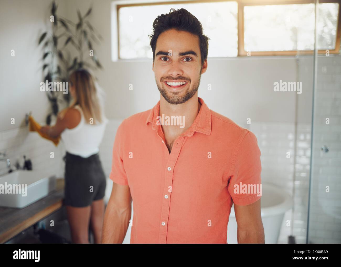 Portrait of a young caucasian couple sharing a bathroom with focus on happy young man smiling showing perfect teeth while looking at the camera in the Stock Photo