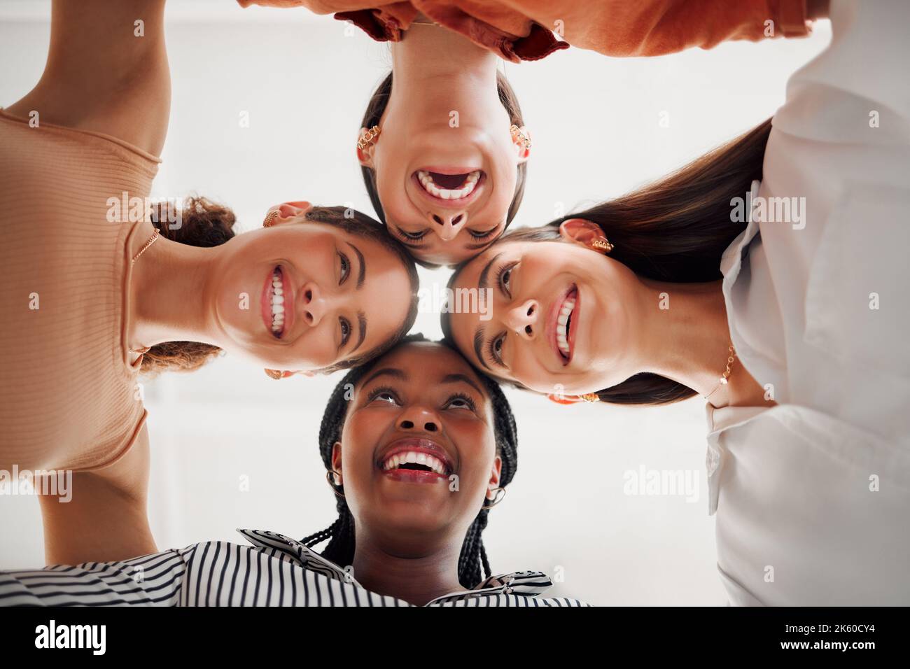 Four happy businesswomen joining their heads together in a circle in an office at work. Diverse group of cheerful businesspeople having fun standing Stock Photo