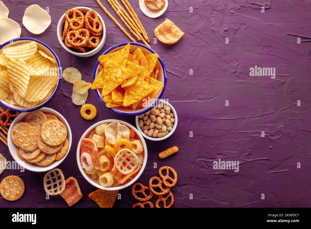 Salty snacks. Potato and tortilla chips, crackers and other appetizers in bowls, overhead flat lay shot with copy space. Party food background Stock Photo