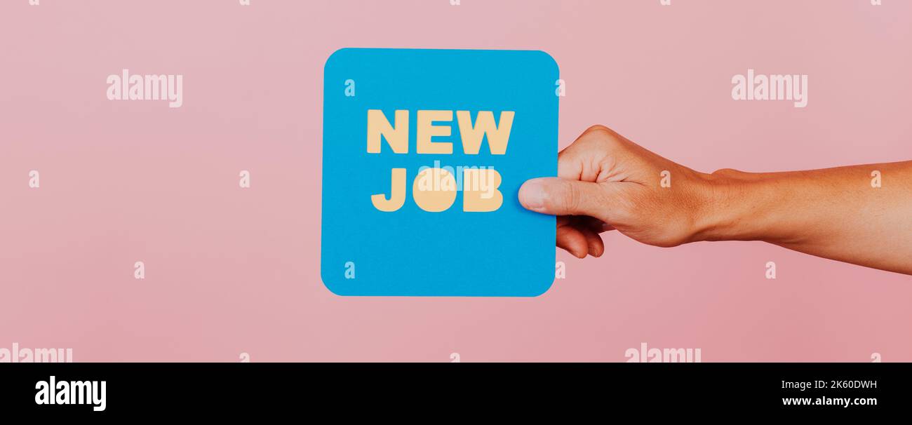 man holding a blue paper speech bubble that reads the text new job, on a pink background, in a panoramic format to use as web banner or header Stock Photo