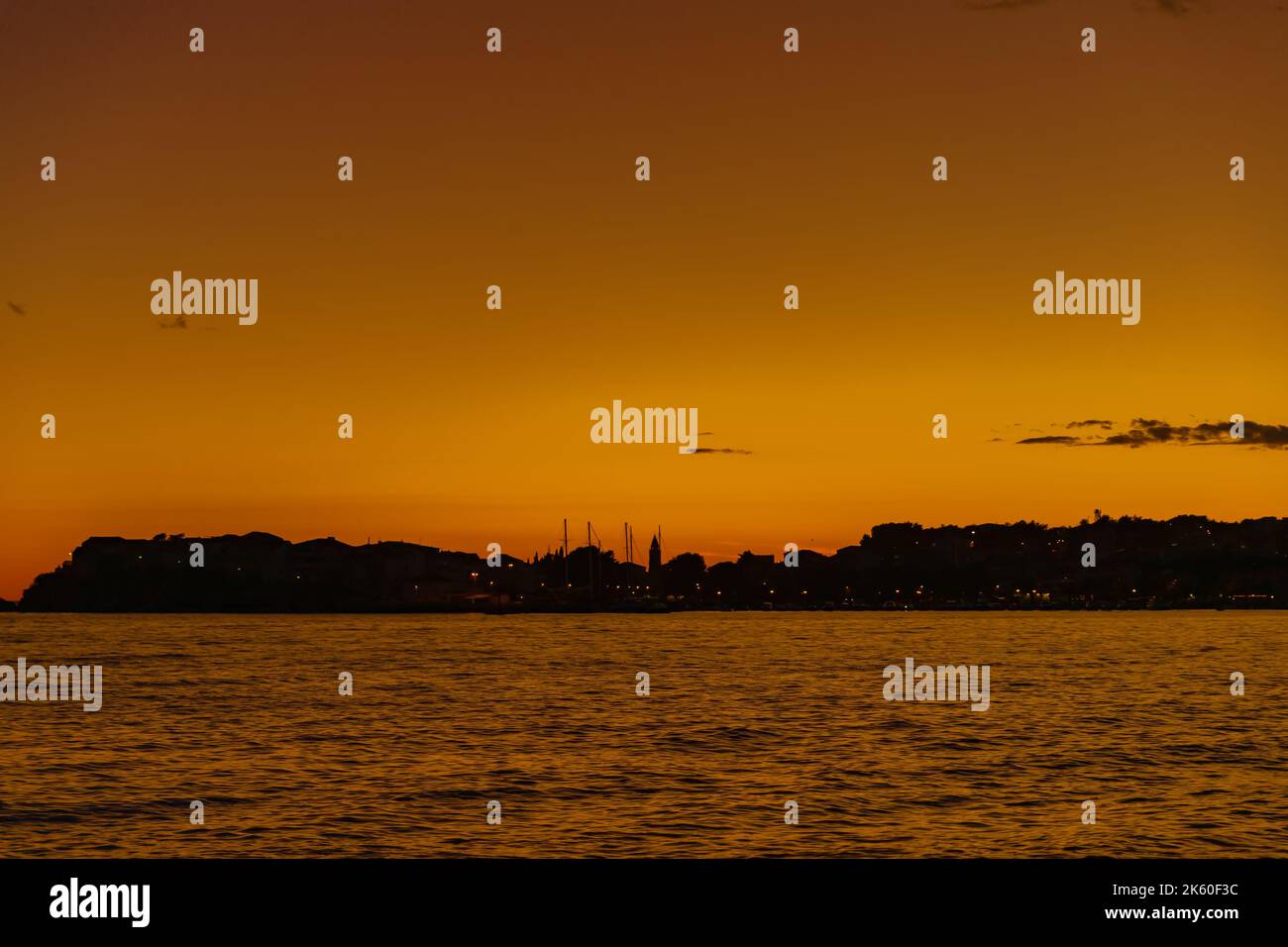 Beautiful panoramic sunset on the sea with silhouettes of bell tower and sailing ships masts on the horizon in Croatia. Stock Photo