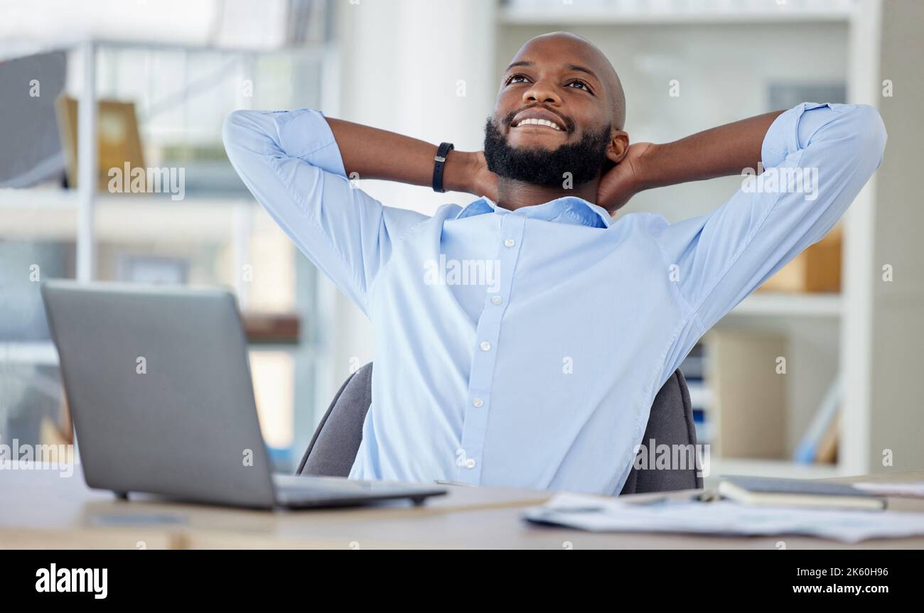 Young African american businessman sitting with his hands behind his back while using a laptop in an office alone at work. Content male businessperson Stock Photo