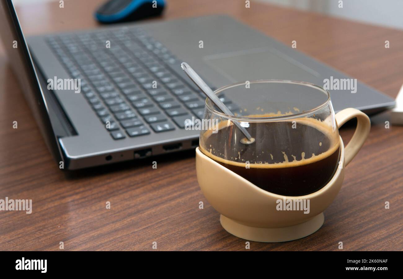 close-up shot of coffee cup next to laptop computer at work table with selective focus Stock Photo