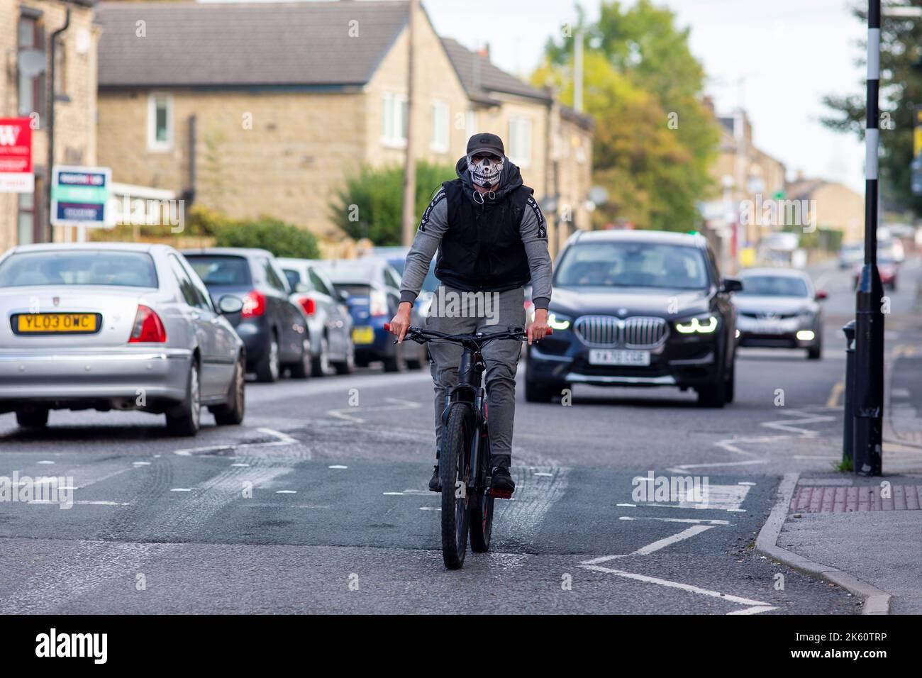 A young man on a mountain bike wearing a skeleton face mask to disguise his appearance and no helmet down the main street of Wyke, Bradford, West Yorkshire, UKCredit: Windmill Images/Alamy Live News Stock Photo