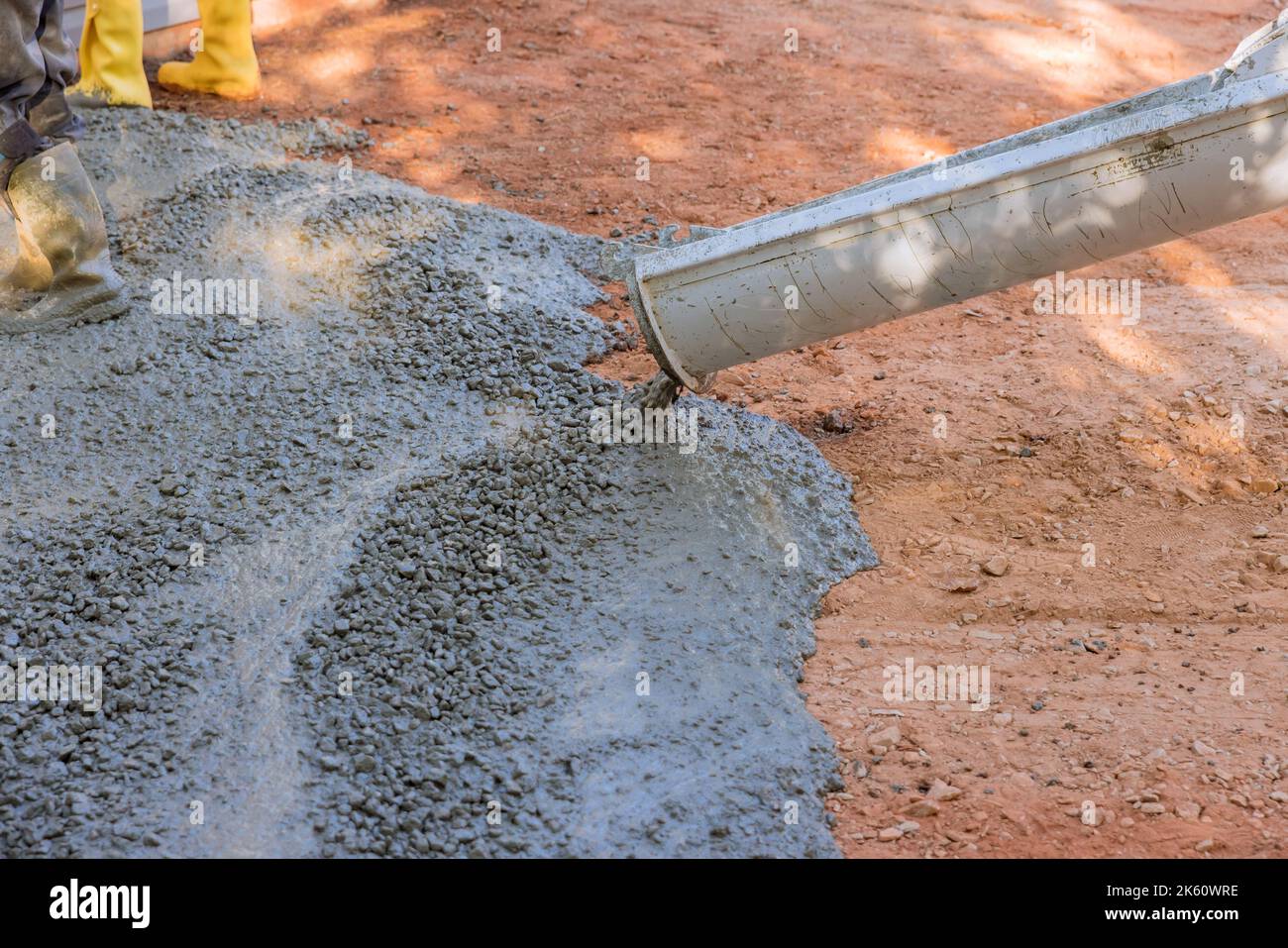 An employee at construction site pouring wet concrete into driveway that is paving over near new