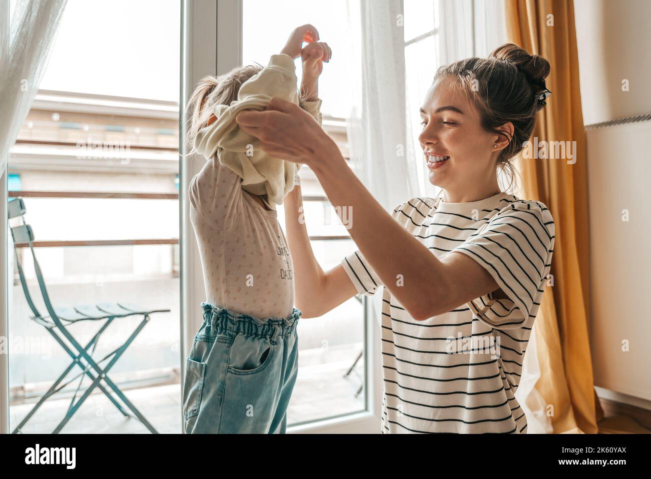 Loving mother dressing her daughter by the window Stock Photo
