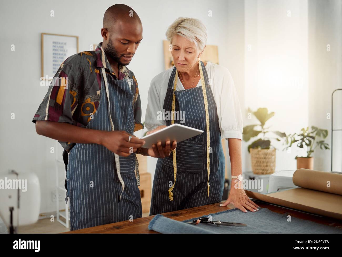 Two designers using a digital tablet while working with material at work. Young african american tailor talking and holding a digital tablet while Stock Photo