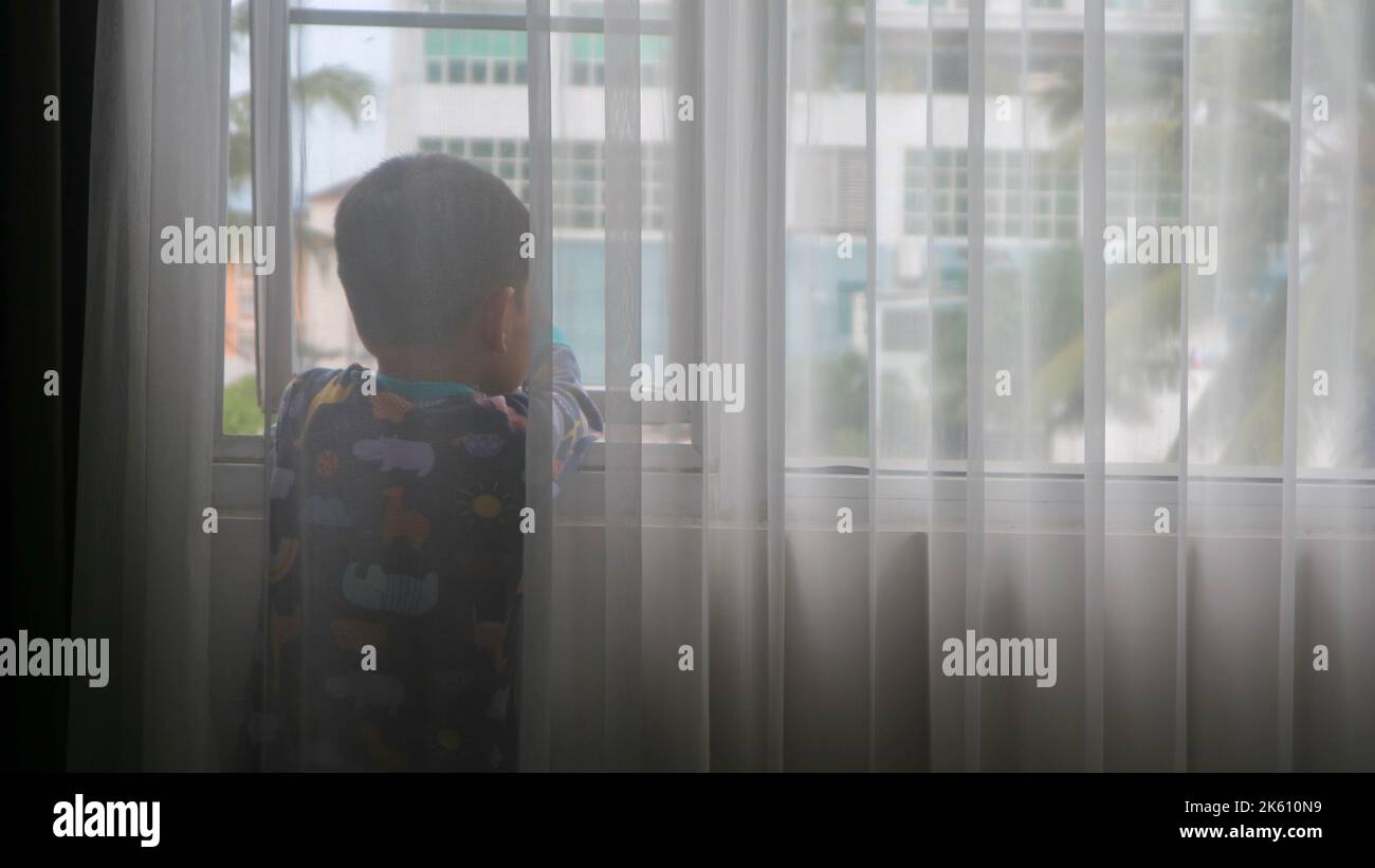 a boy behind the curtain is looking at the beautiful view in the window ...