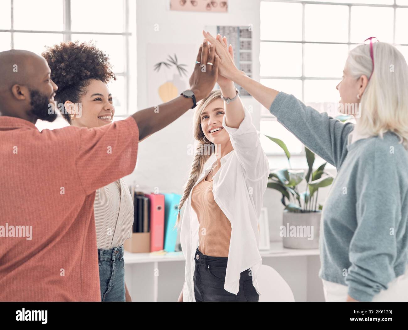 Group of four cheerful diverse businesspeople giving each other a high five in an office at work. Business professionals having fun joining their Stock Photo