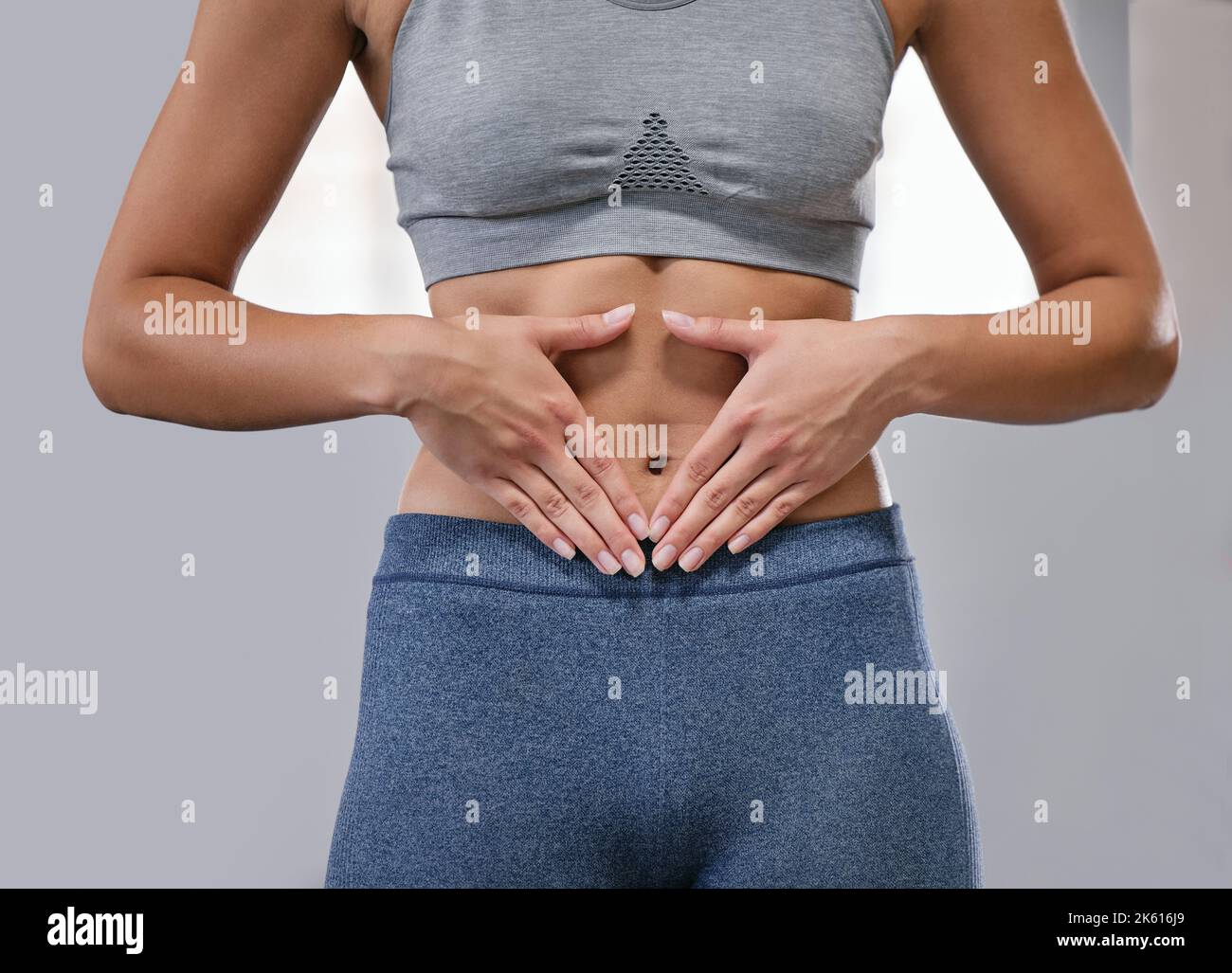 Closeup of one fit caucasian woman framing hands around her slim belly to show weight loss while exercising against a grey background. Female athlete Stock Photo