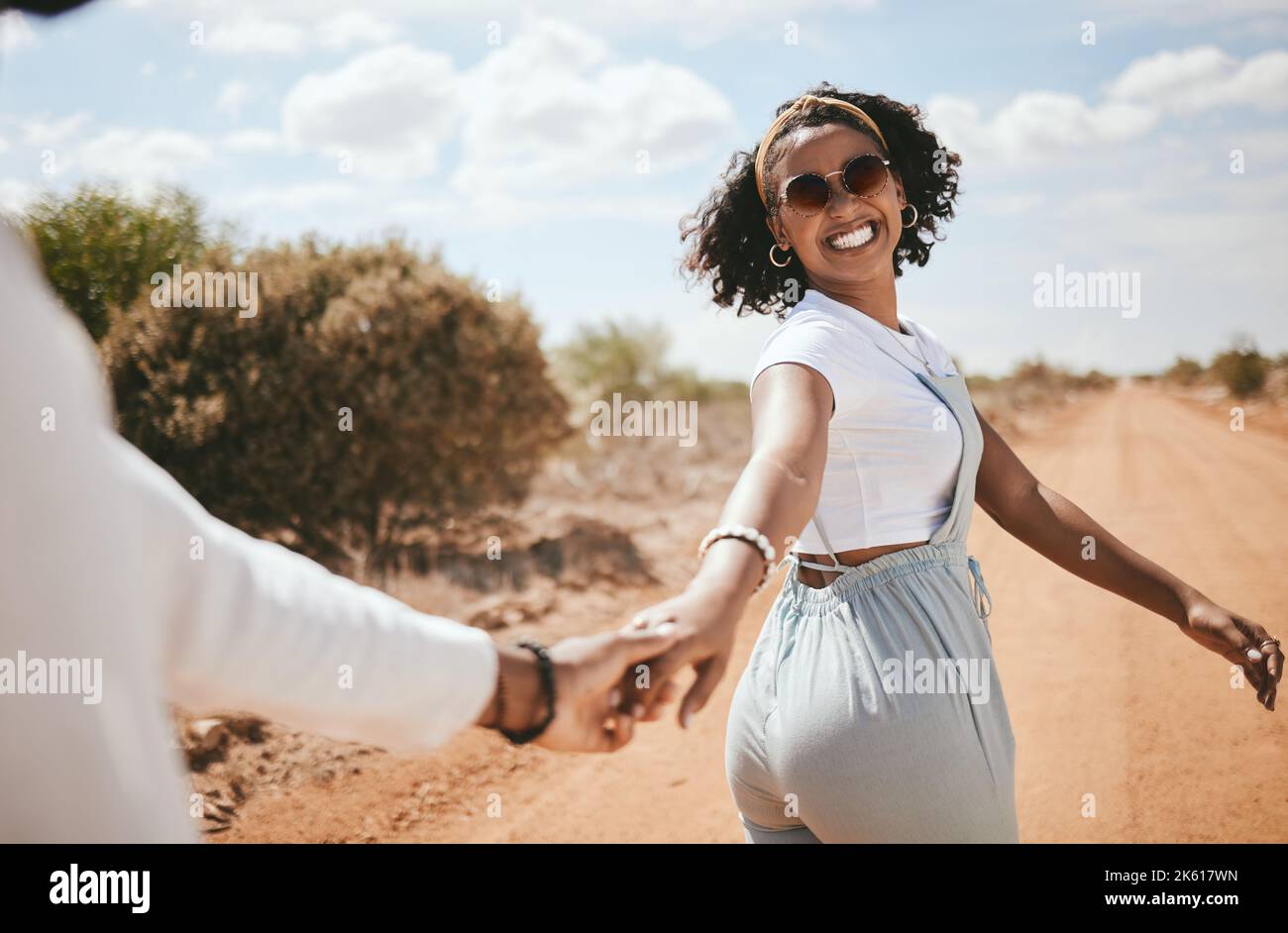 Couple, walking and nature with a black woman and man outdoor holding hands on a sand road in a dessert together. Travel, love and romance with a Stock Photo