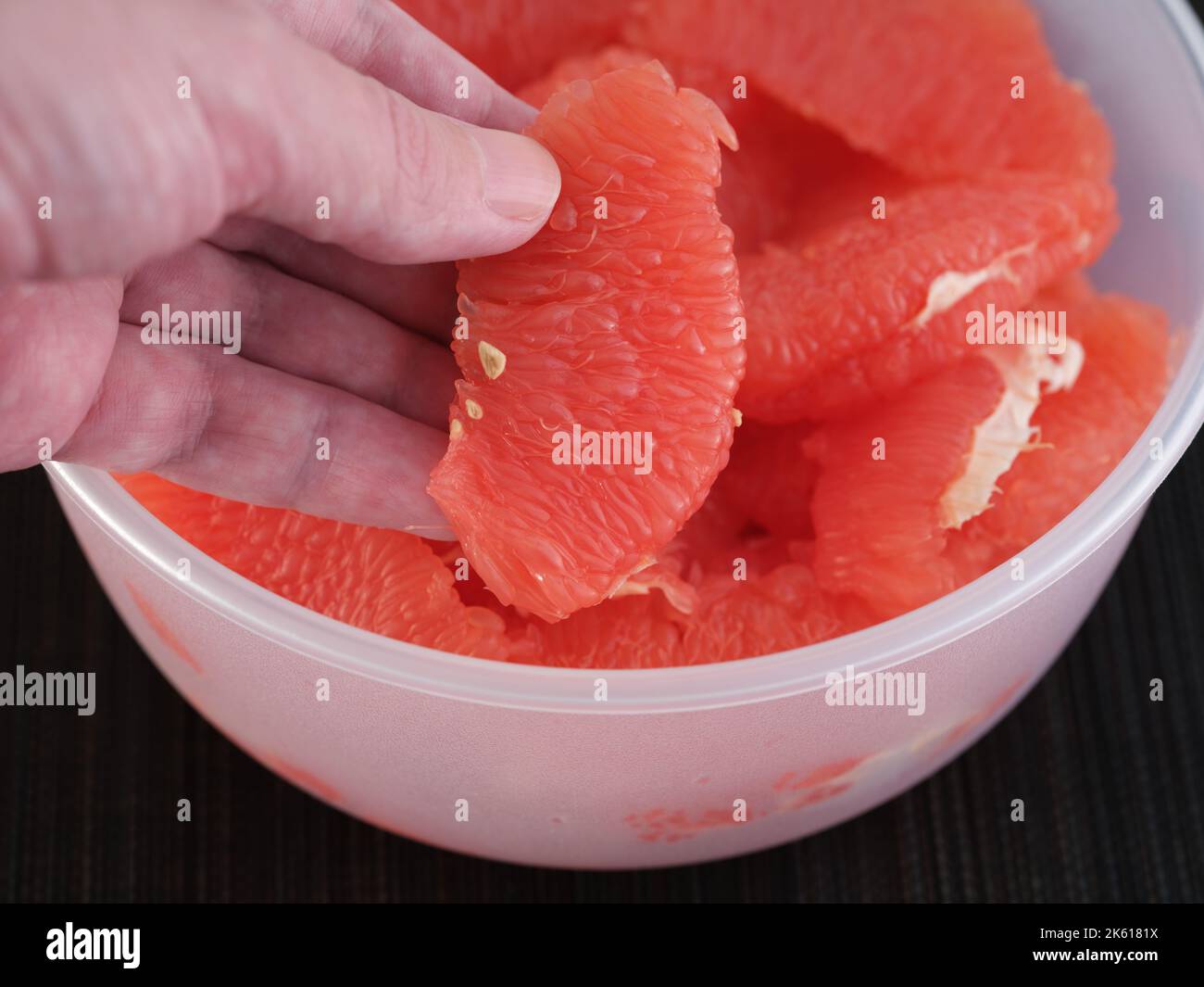 A man taking a grapefruit slice out of a bowl of grapefruit slices. Close up. Stock Photo