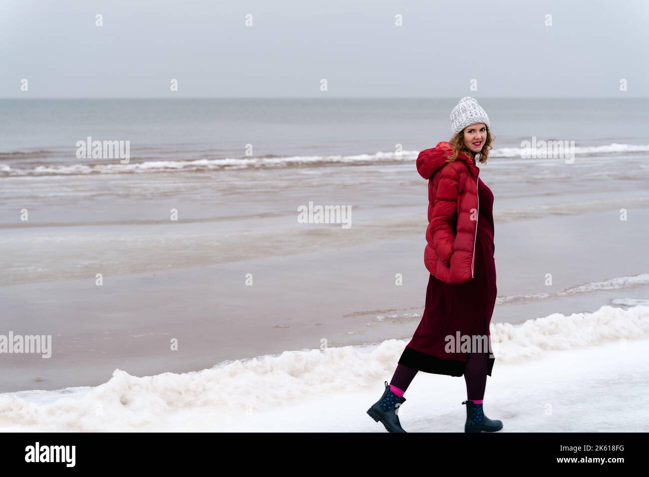 A woman in a red jacket and a red knitted dress walks in winter along the Baltic sea. Jurmala, Latvia Stock Photo