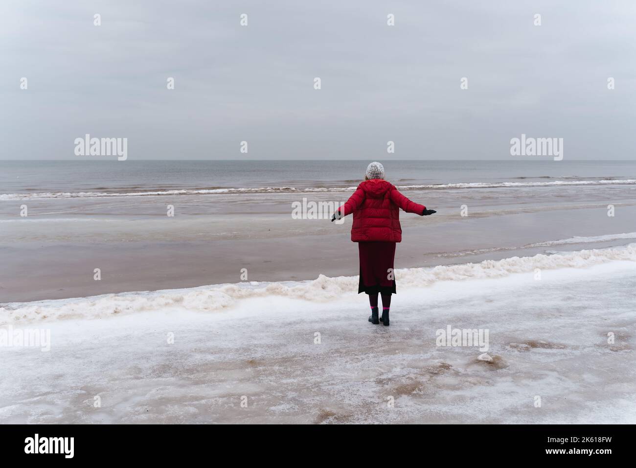 A woman stands looking at the Baltic sea spreading her arms to the sides, the view from behind in Jūrmala, Latvia Stock Photo