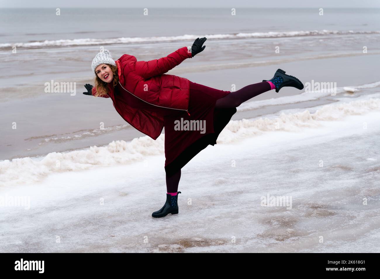 Cheerful woman on the beach in the arabesque pose in winter. Stock Photo