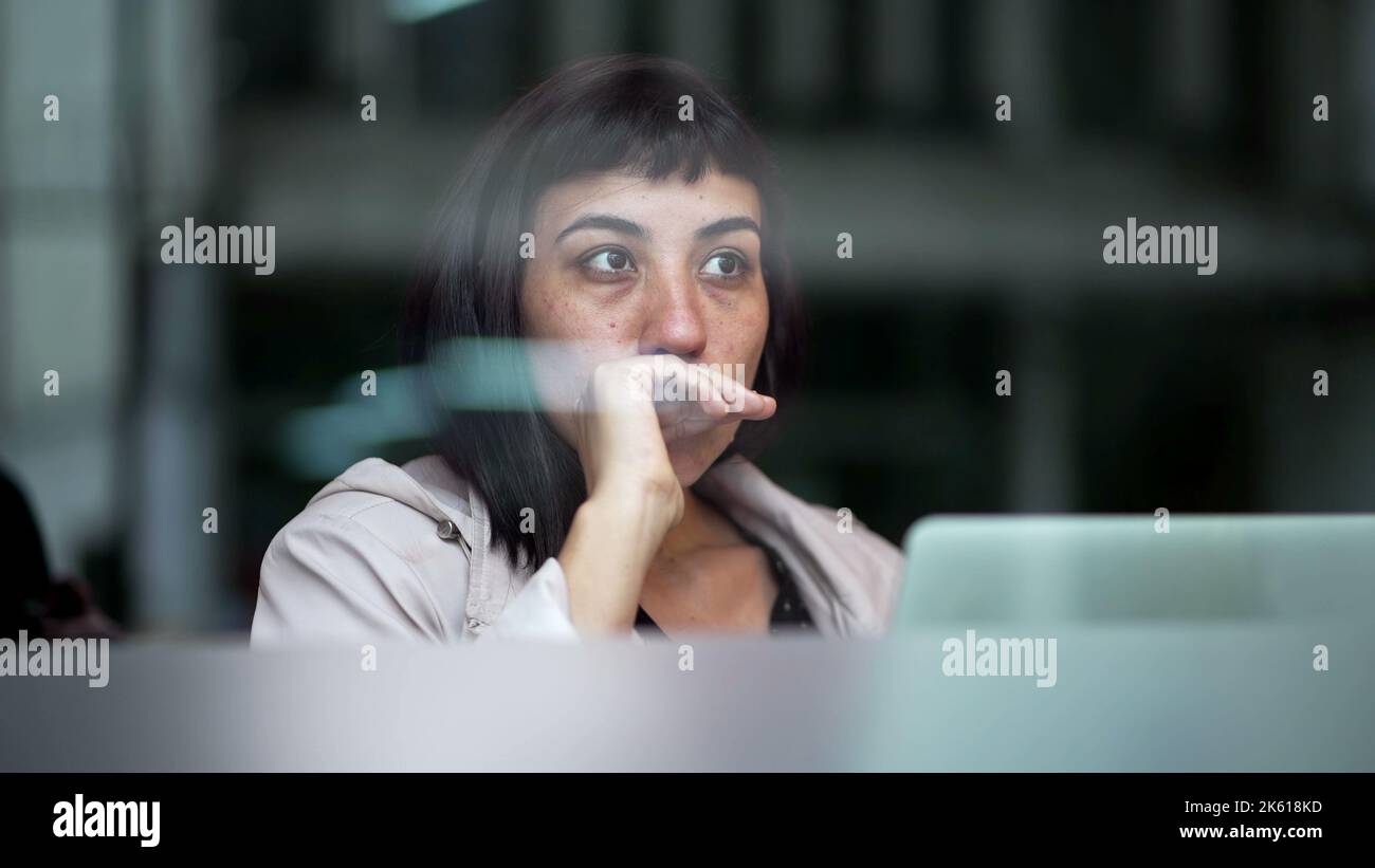 Pensive young woman thinking while working in front of laptop seen ...