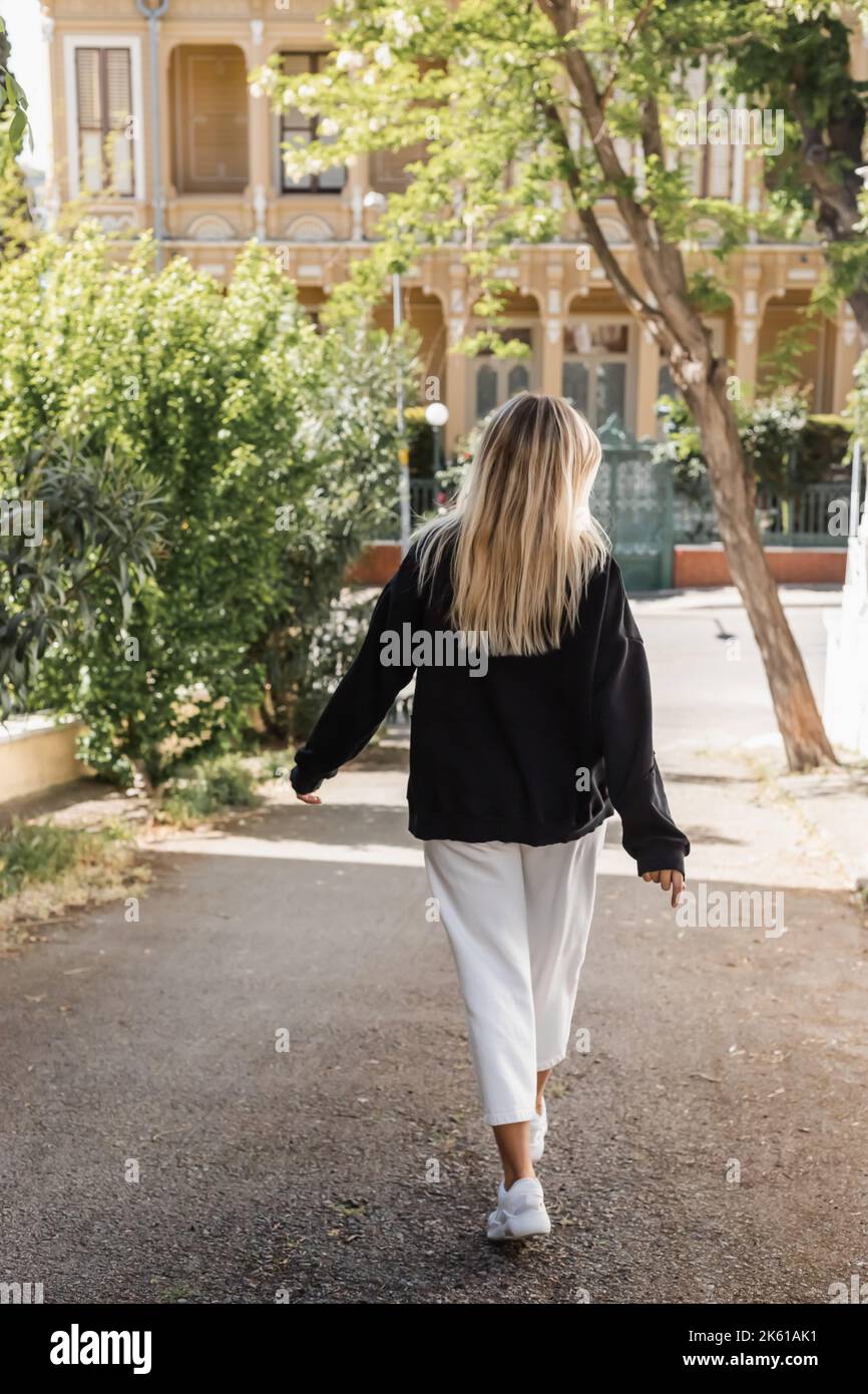 Back View Of Young Blonde Woman In Stylish Outfit Walking On Street In back-view-of-young-blonde-woman-in-stylish-outfit-walking-on-street-in