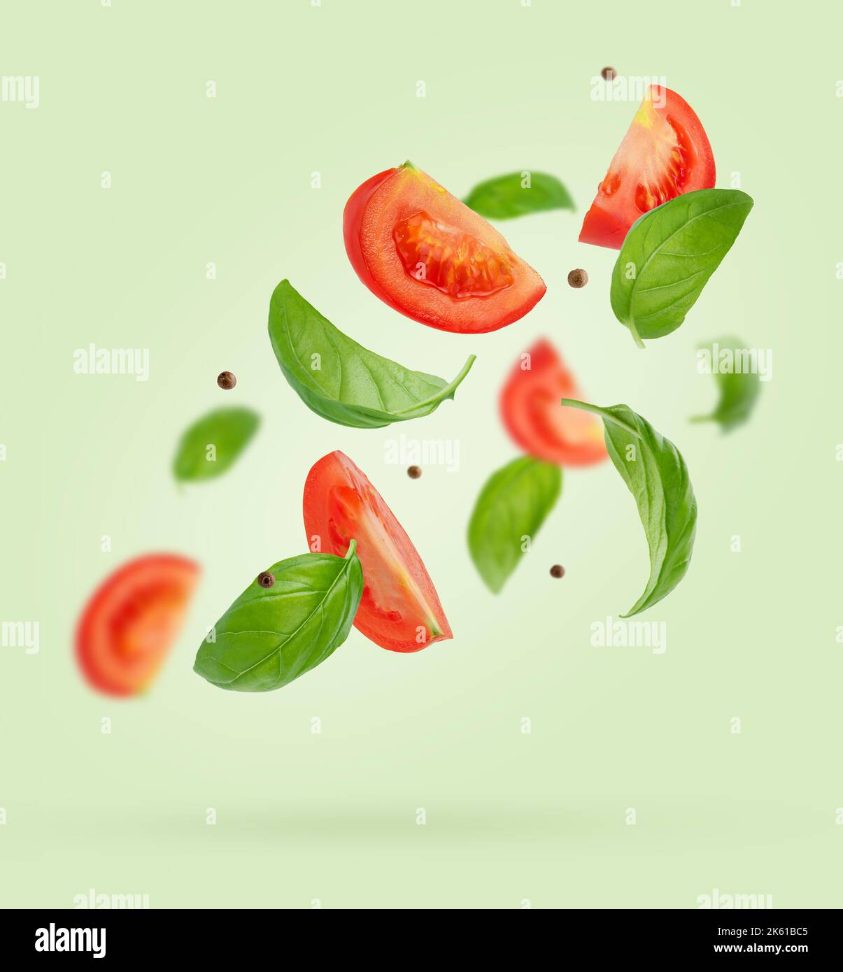 Flying ingredients of tomatoes, basil, black pepper on green background. Italian food Stock Photo