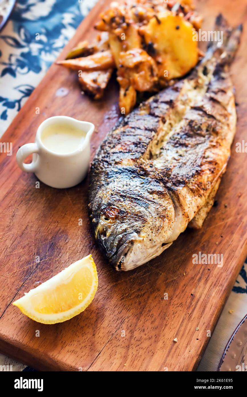 Grilled sea bream served on a rustic wooden board with a side of sweet